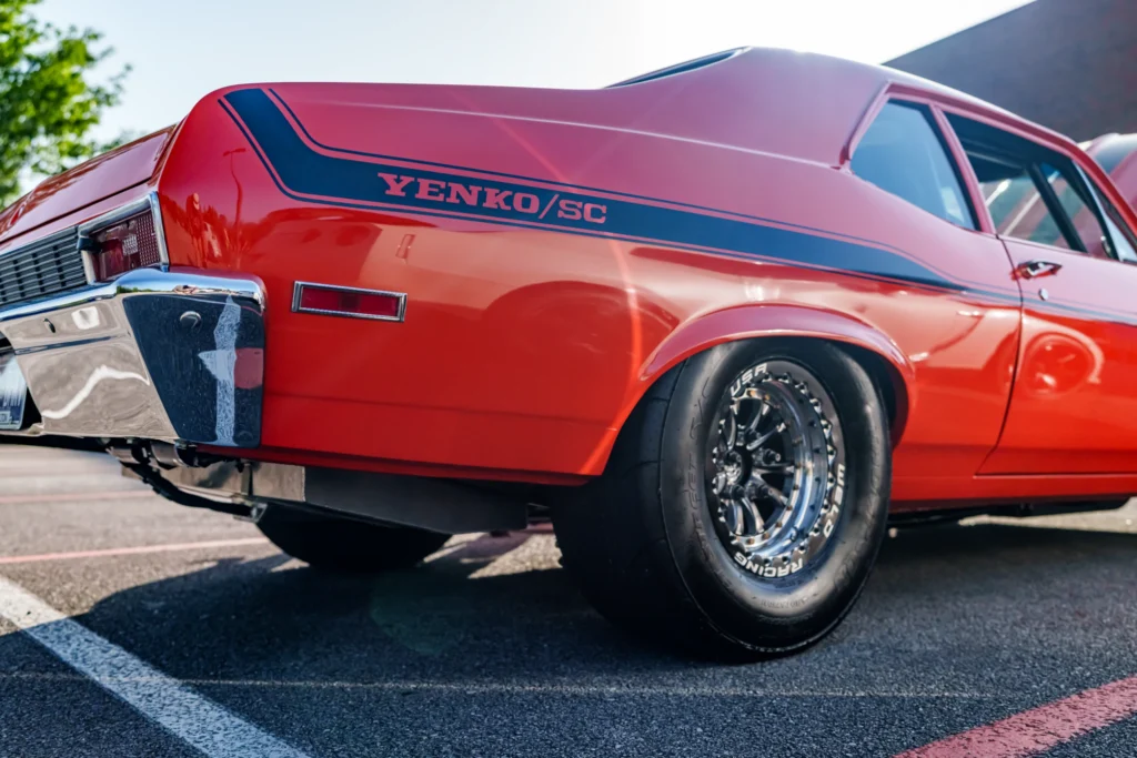 Red Yenko/SC muscle car with black stripe and racing tires parked in a lot under clear sky