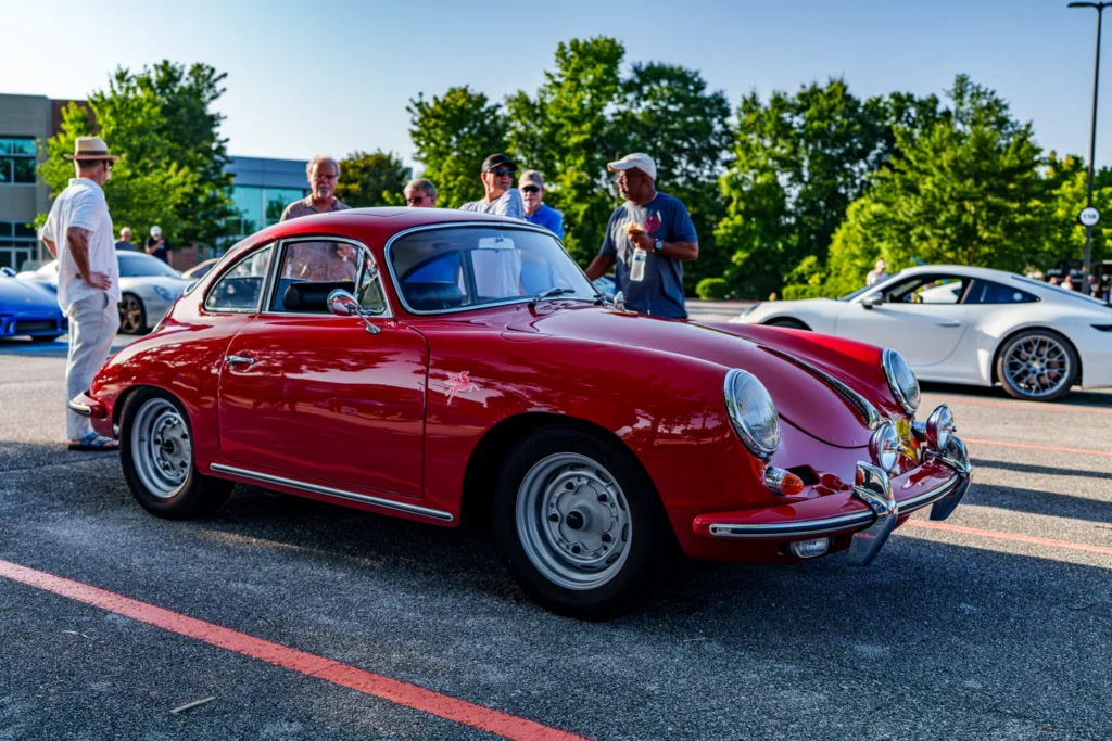 Red Porsche 356 coupe parked at an outdoor car event with people and other cars in the background