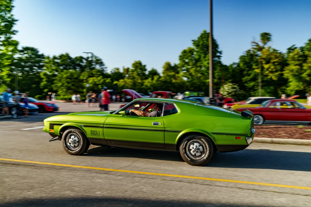 Bright green Ford Mustang Mach 1 driving in a parking lot with people and other cars in the background