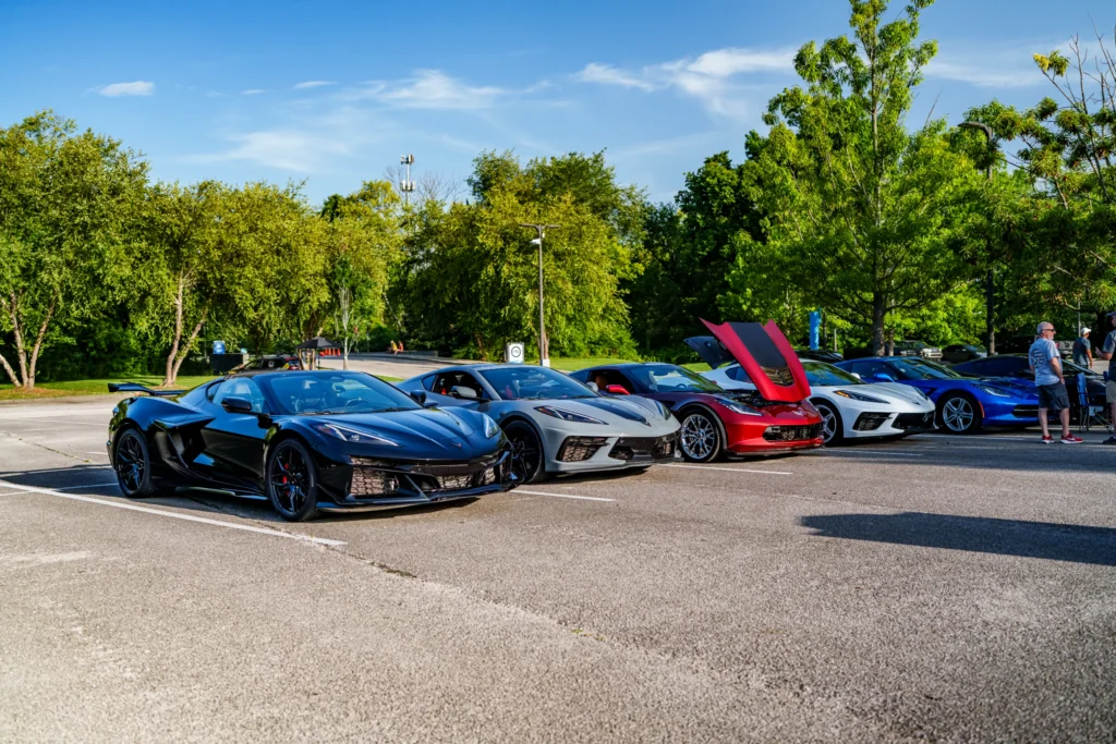 Black, gray, red, white, and blue Chevrolet Corvette sports cars parked in a row outdoors with people nearby