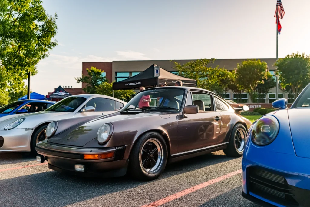 Three Porsche 911 cars parked side by side at an outdoor car event with trees and tents in the background