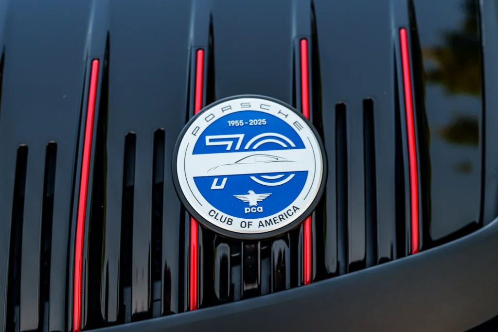 Close-up of blue and white Porsche Club of America emblem on black car hood with red accent lines