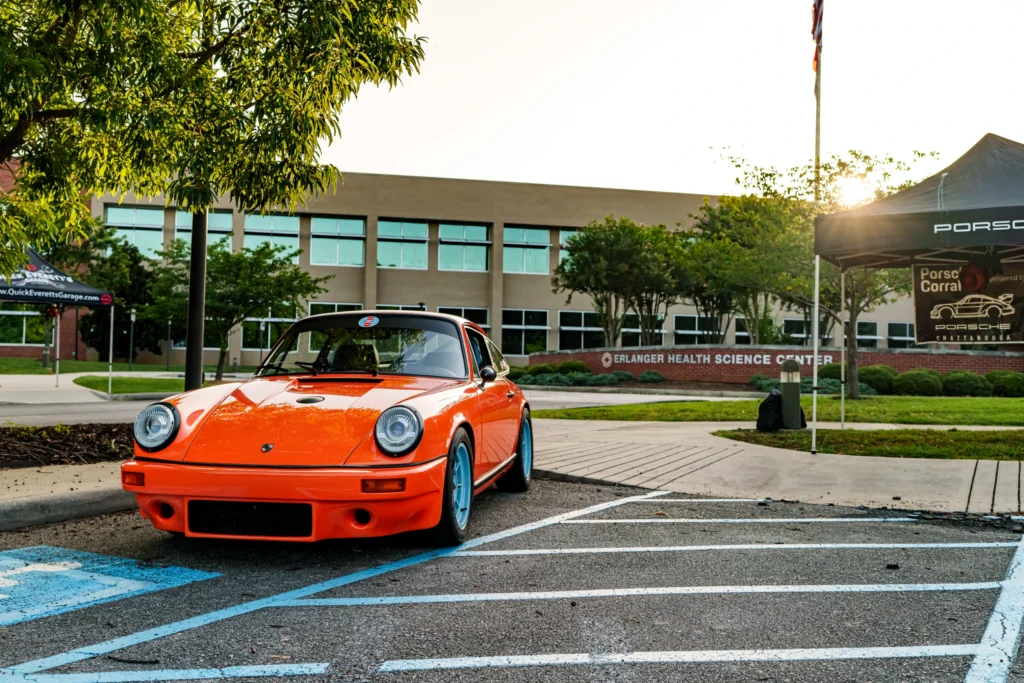 Orange Porsche 911 with blue wheels parked in a lot near the Erlanger Health Science Center at a car event