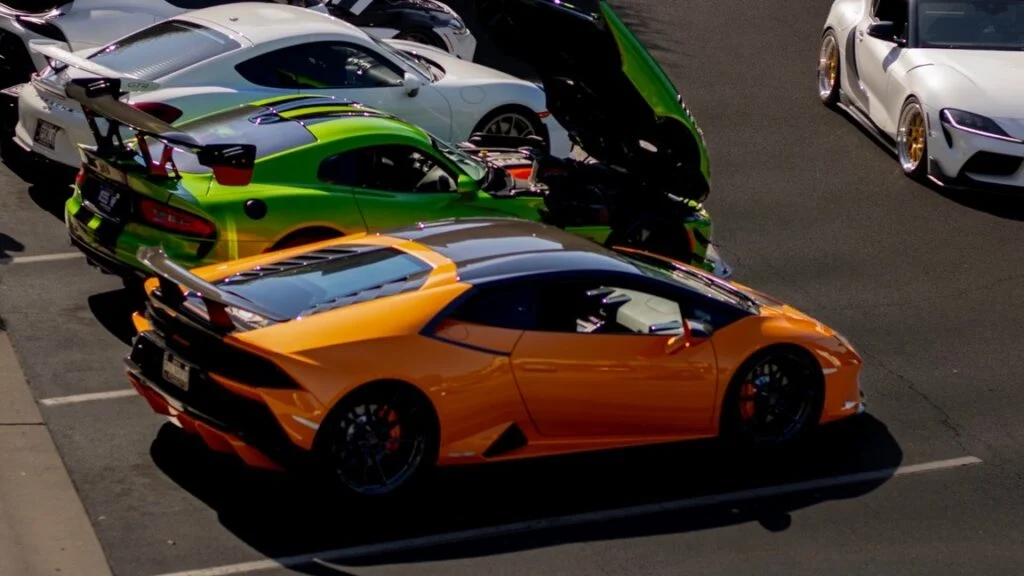 Orange Lamborghini Huracán and green Dodge Viper parked side by side with Porsche 911 and Toyota Supra nearby at a car event 