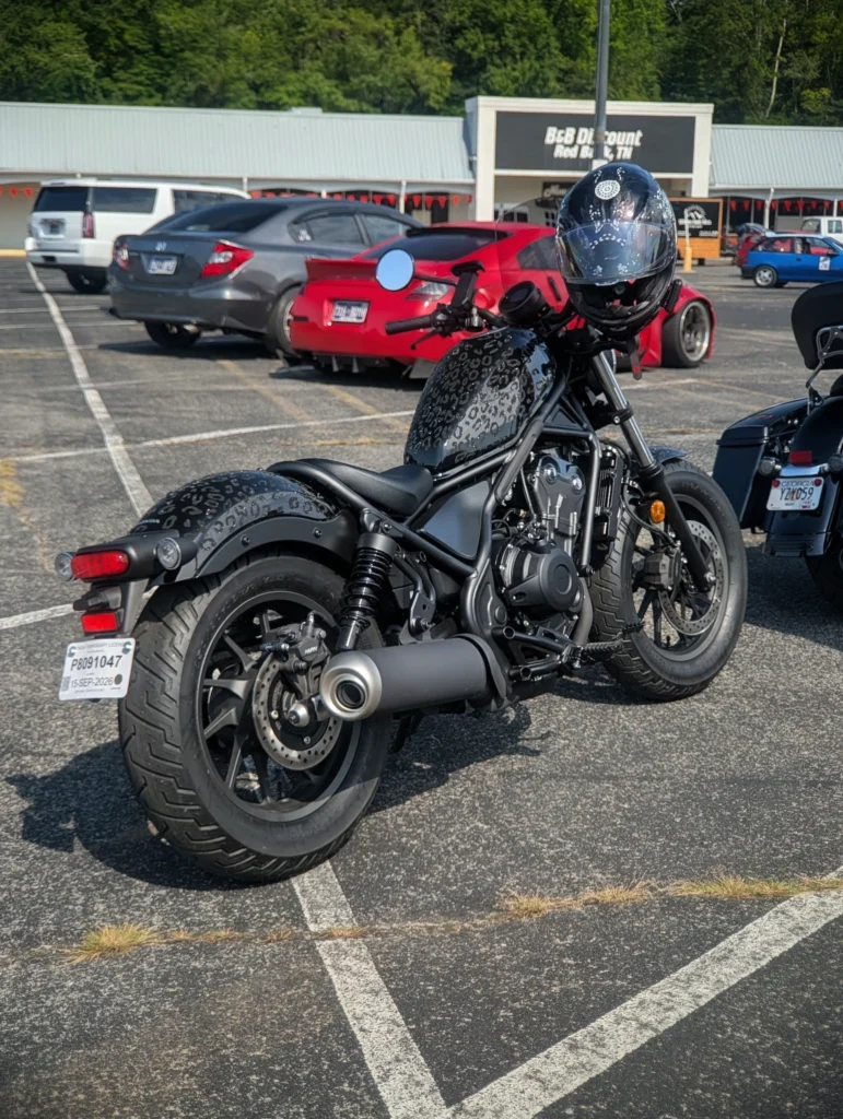 Black Honda Rebel cruiser with patterned tank and helmet parked in a lot with several cars in the background