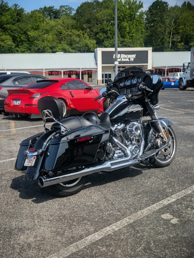 Black Harley-Davidson motorcycle parked in a parking lot with a red sports car in the background