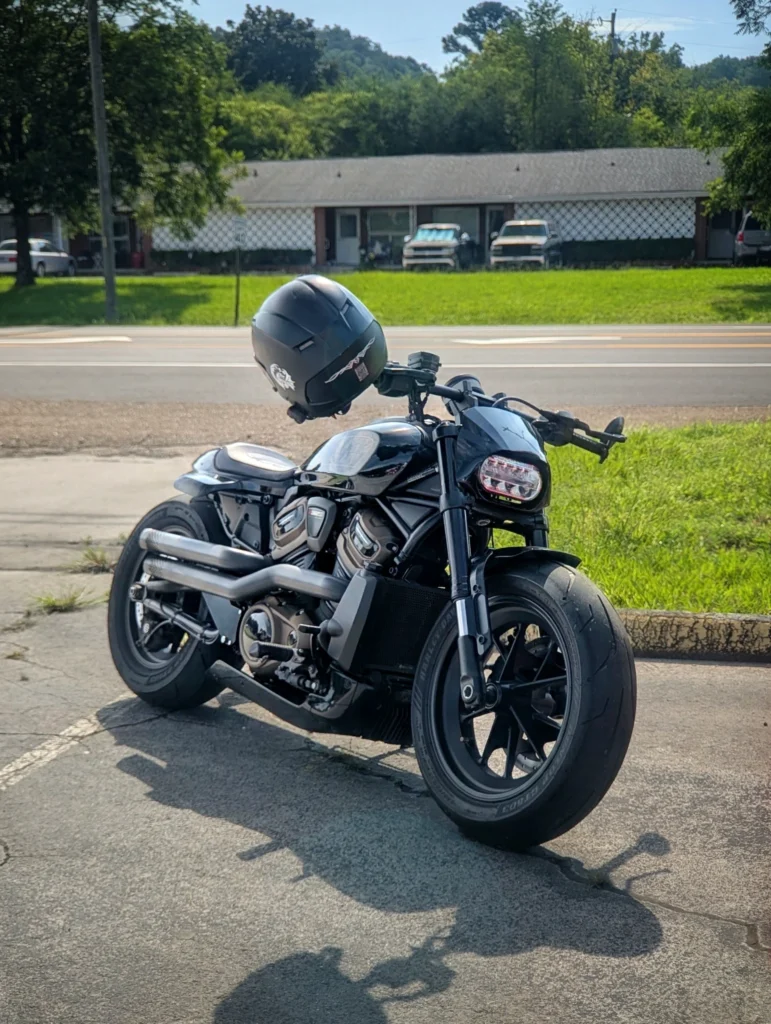 Black Harley-Davidson motorcycle parked on pavement with black helmet resting on handlebars, grassy area and buildings in bac