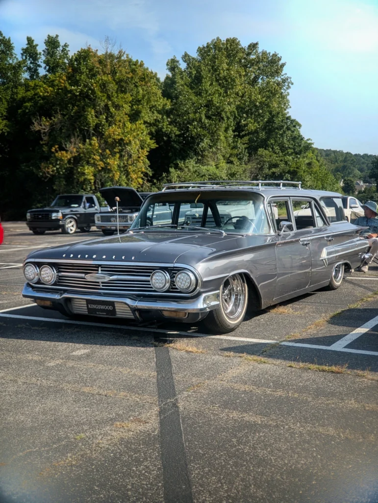 Gray Chevrolet Kingswood station wagon with roof rack parked outdoors, surrounded by other vehicles and trees in the backgrou