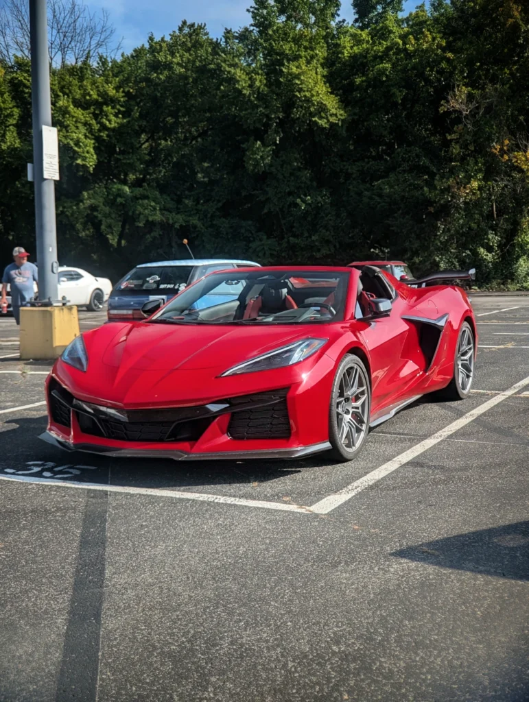 Red Chevrolet Corvette convertible parked in a lot with trees and other cars in the background