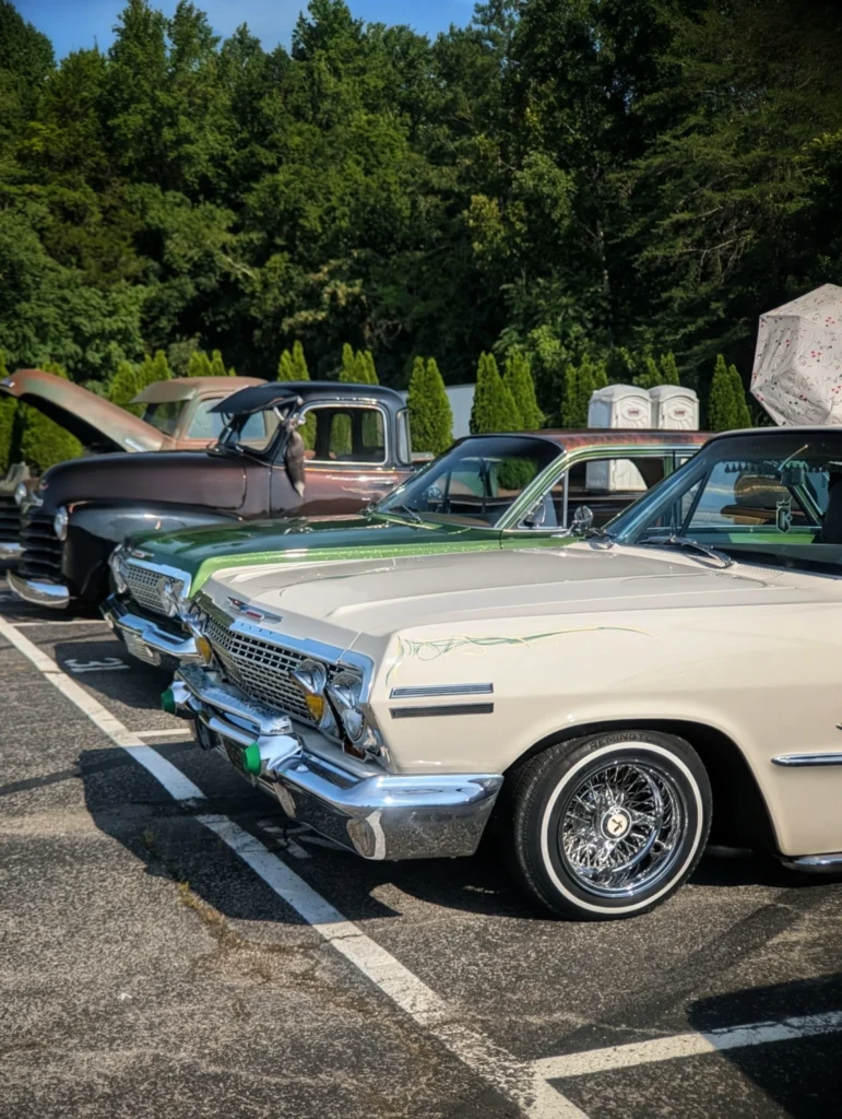White Chevrolet Impala with green top parked next to two vintage pickup trucks at outdoor car event