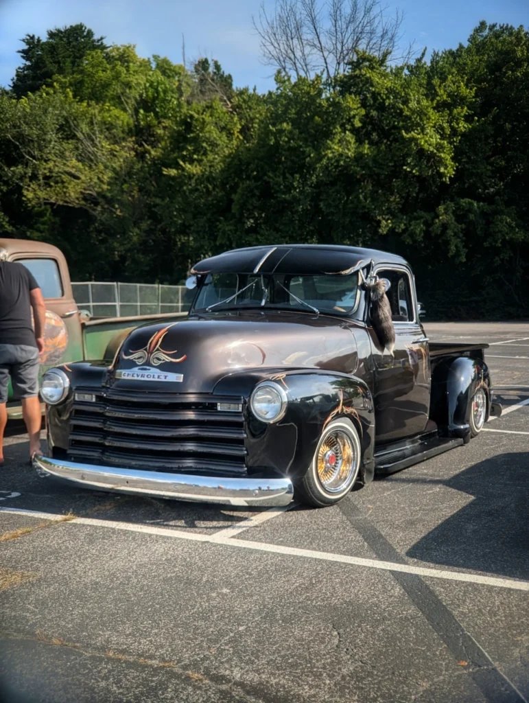 Chevrolet 3100 with pinstriping and a wind visor parked in a lot with trees in the background