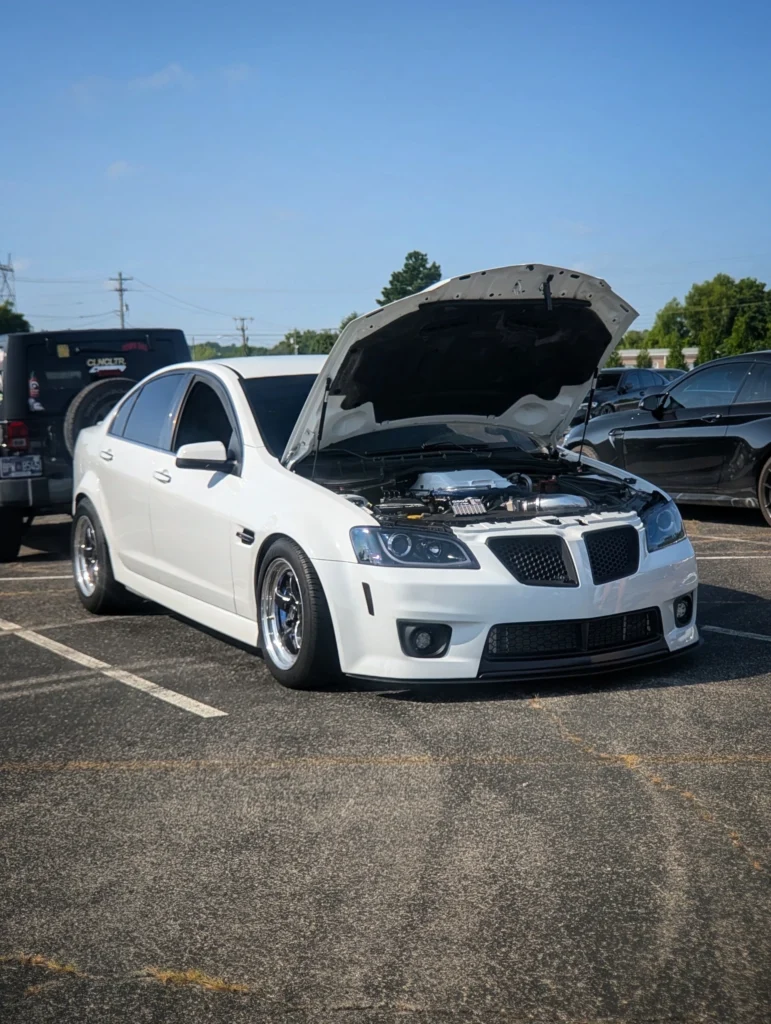 White Pontiac G8 sedan with hood open in a parking lot during car event