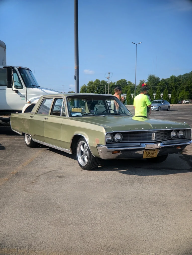 Light green Chrysler Newport parked in a lot with two men standing nearby under a clear blue sky.
