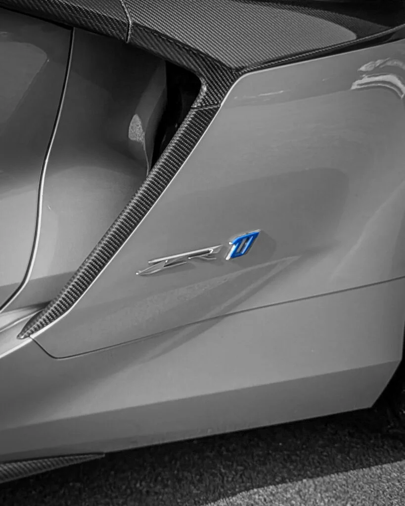 Gray Corvette ZR1 badge and carbon fiber vent detail on car body at outdoor event
