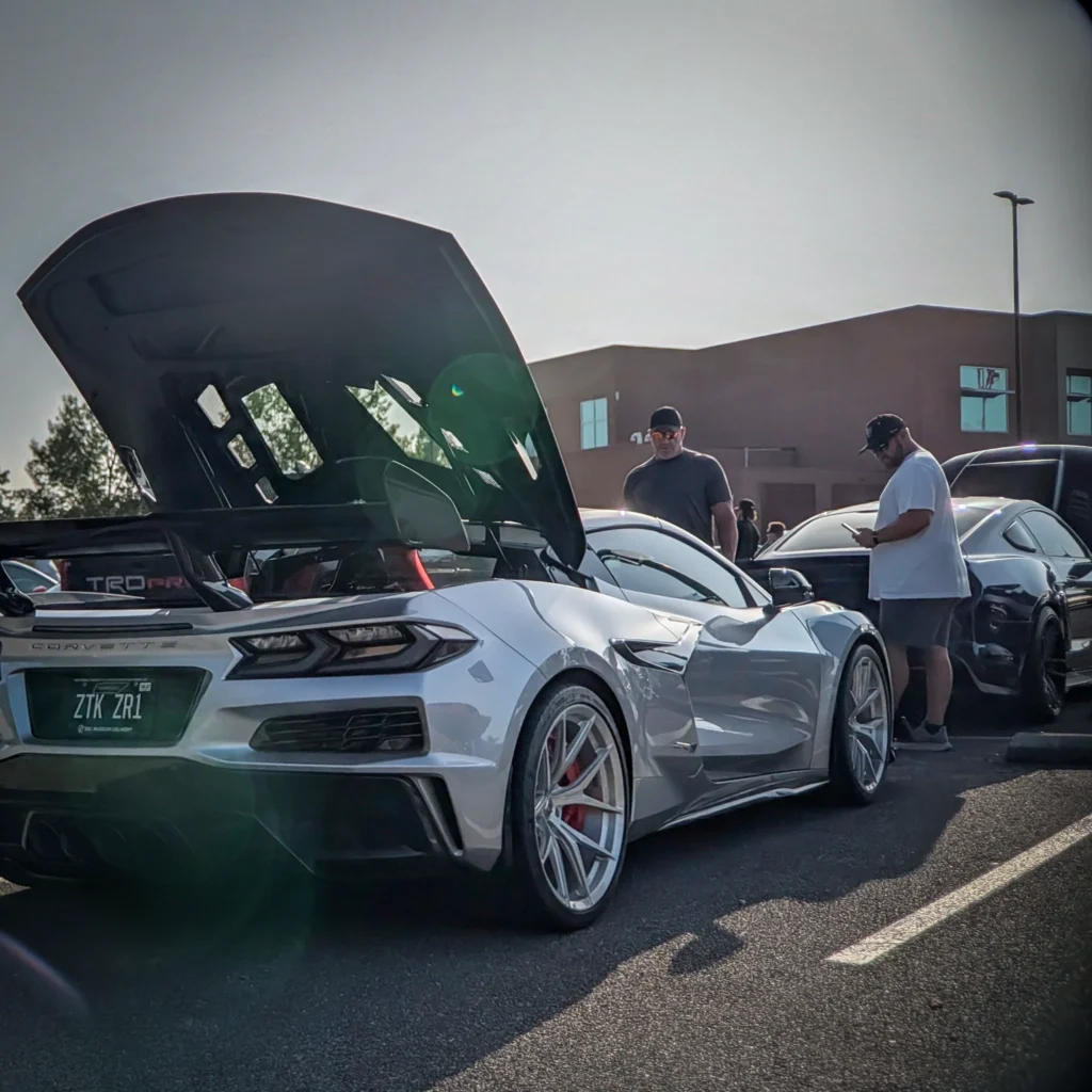 White Chevrolet Corvette ZR1 with open hood and two men nearby in a parking lot at car event