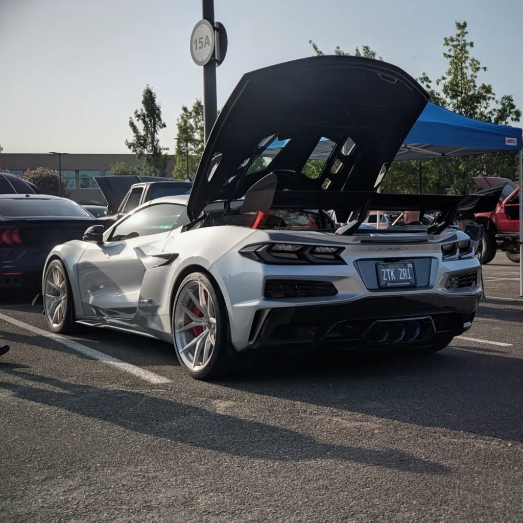 White Chevrolet Corvette ZR1 with hatch open parked at a car event with other cars and a blue canopy in the background