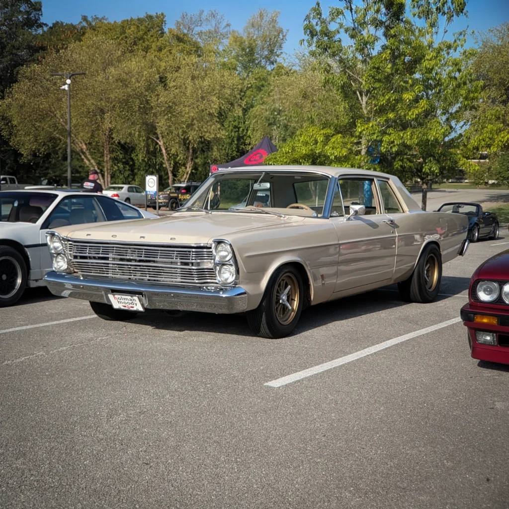 Beige Ford Galaxie parked in a lot with other cars and trees in the background on a clear day