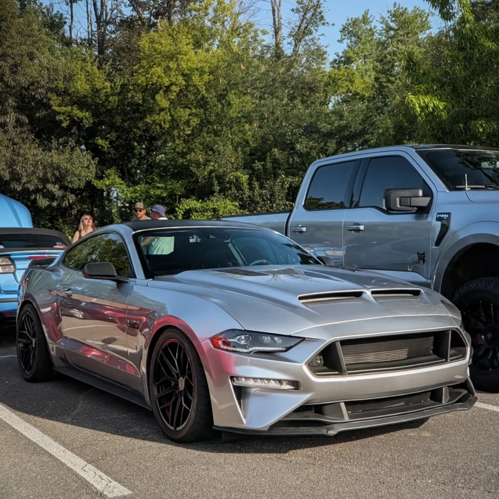 Silver Ford Mustang GT parked outdoors with trees and people in background