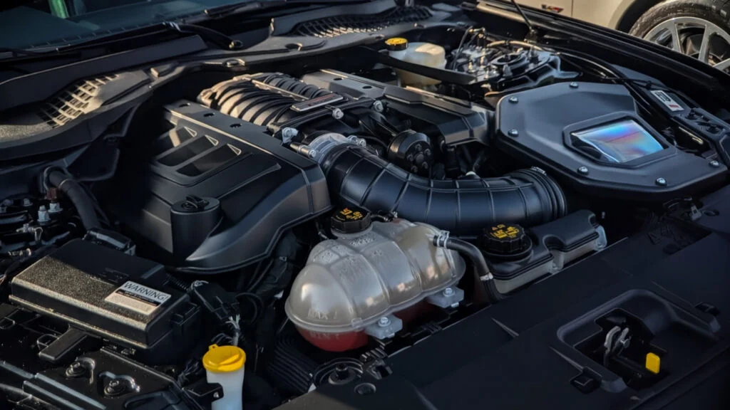 Engine bay of a Ford Mustang showing the intake manifold and coolant reservoir with visible fluid level.