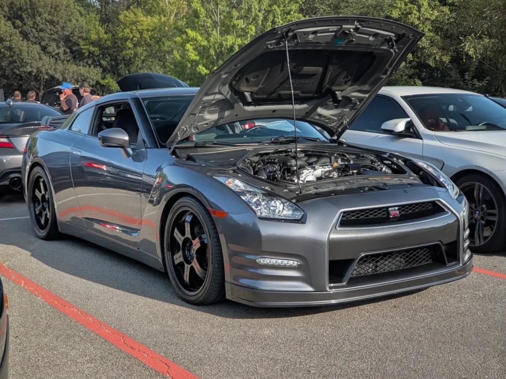 Silver Nissan GT-R with hood open showing engine at an outdoor car meet