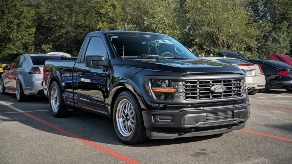 Black Ford pickup truck parked at a car event with other vehicles under trees