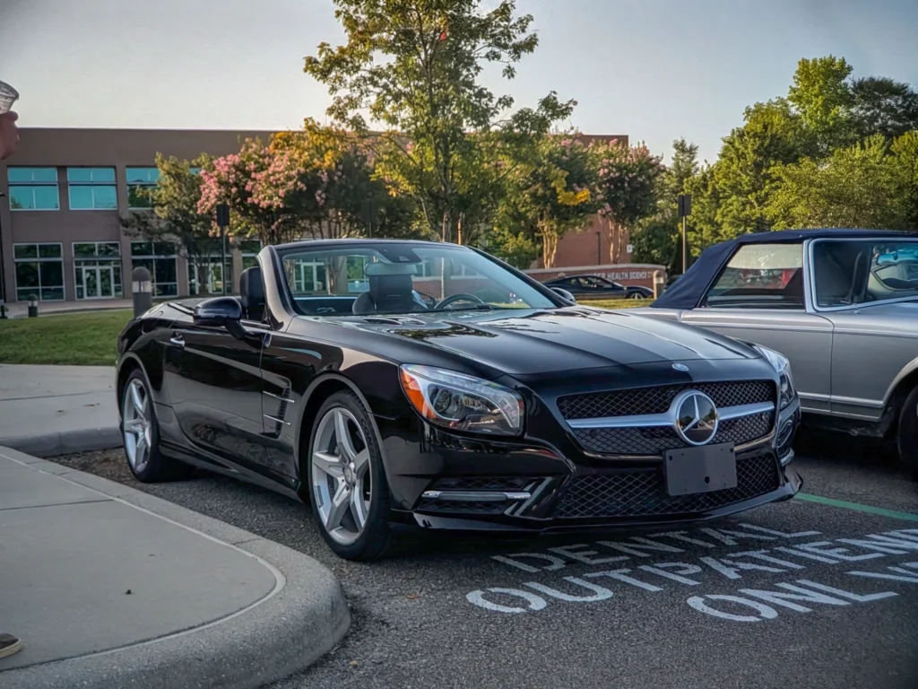 Black Mercedes-Benz SL550 Roadster parked outdoors next to a silver convertible with trees and building in background