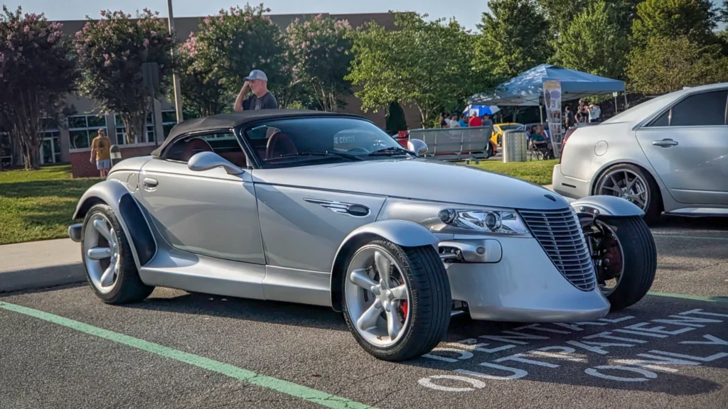 Silver Plymouth Prowler convertible parked at an outdoor car event with people and trees in the background