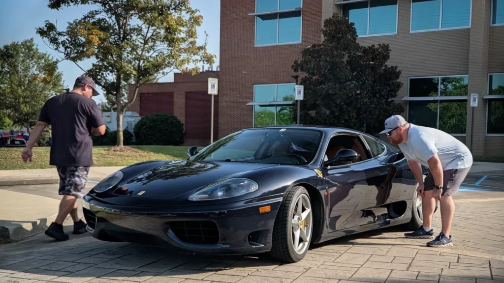 Black Ferrari 360 Modena parked outdoors near a building with two men inspecting the car