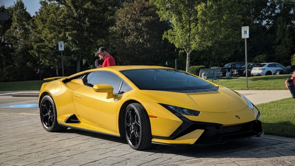 Yellow Lamborghini Huracán parked on pavement near grass and trees with people standing nearby