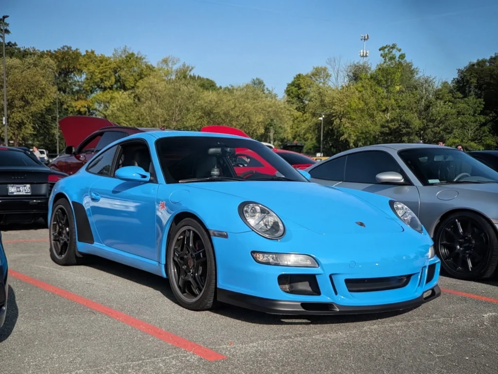 Light blue Porsche 911 GT3 parked in an outdoor lot with other cars and trees in the background