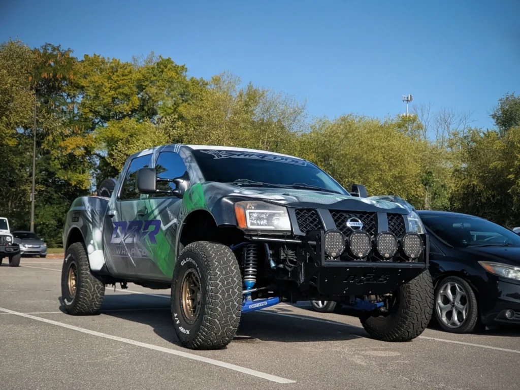 Green and black Nissan pickup truck with off-road modifications parked in a lot with trees in the background