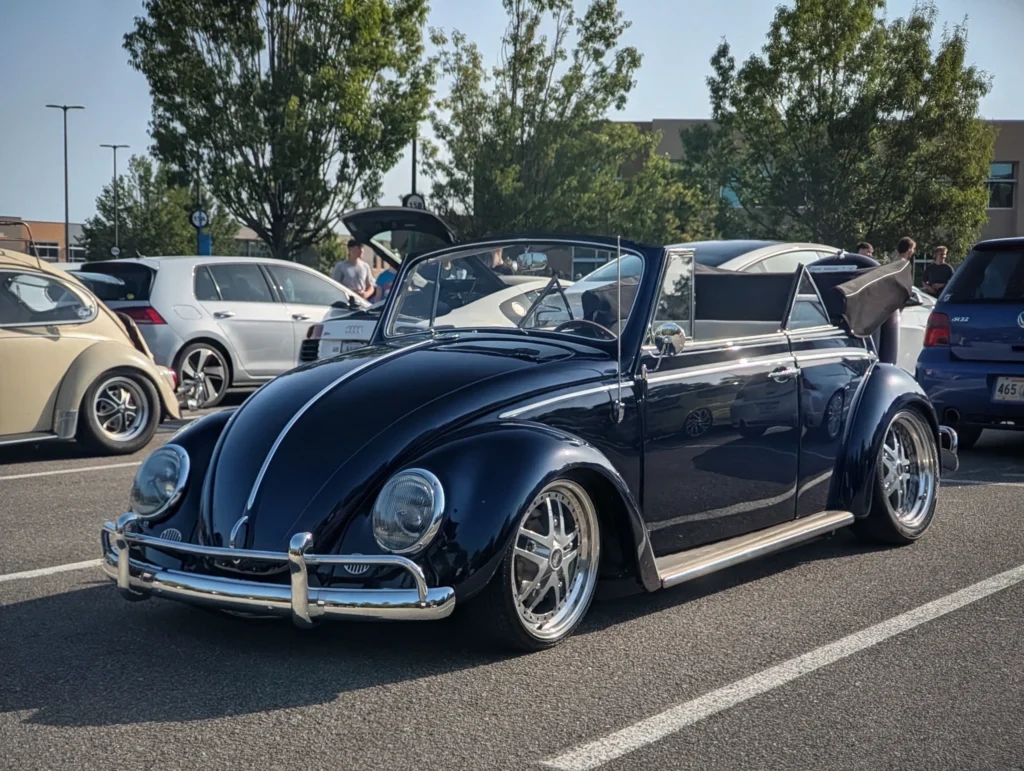 Black Volkswagen Beetle convertible in a parking lot with other vehicles and people in background