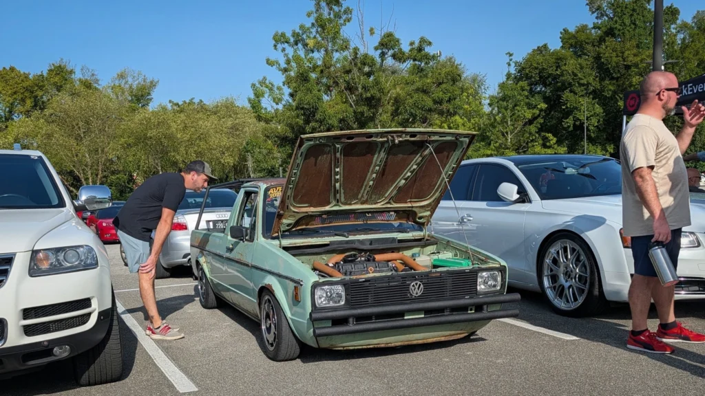 Green Volkswagen pickup truck with hood open at outdoor car event with people inspecting vehicles
