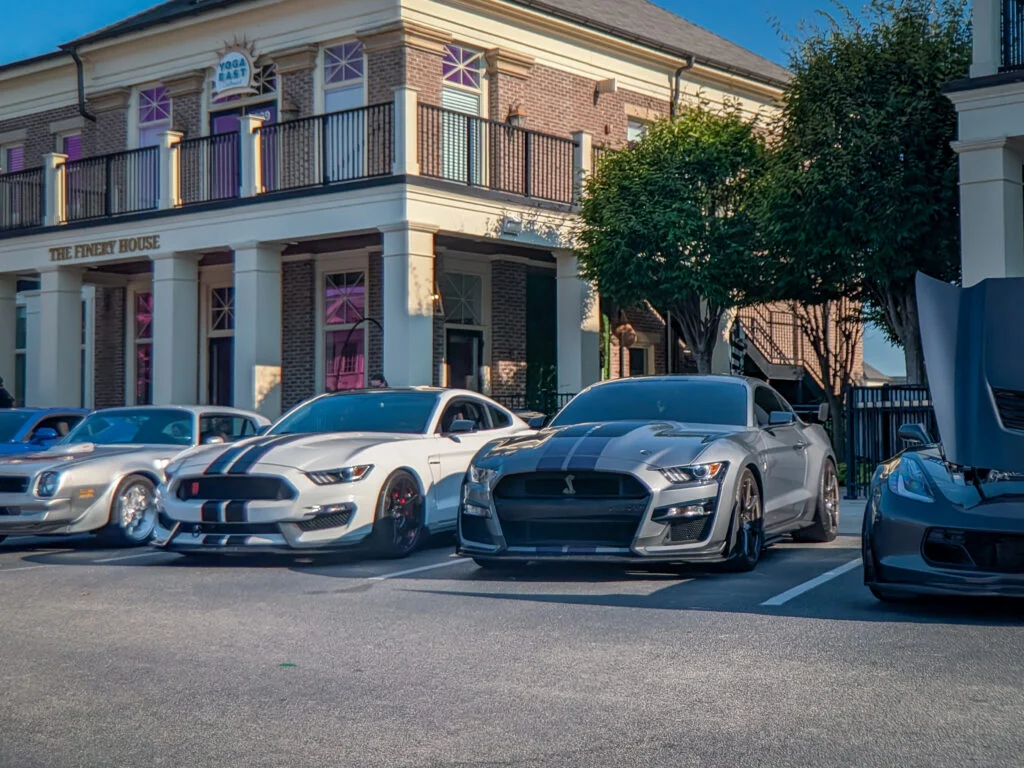 Silver and white Ford Mustang Shelby GT500 and GT350R cars parked side by side in front of a brick building.