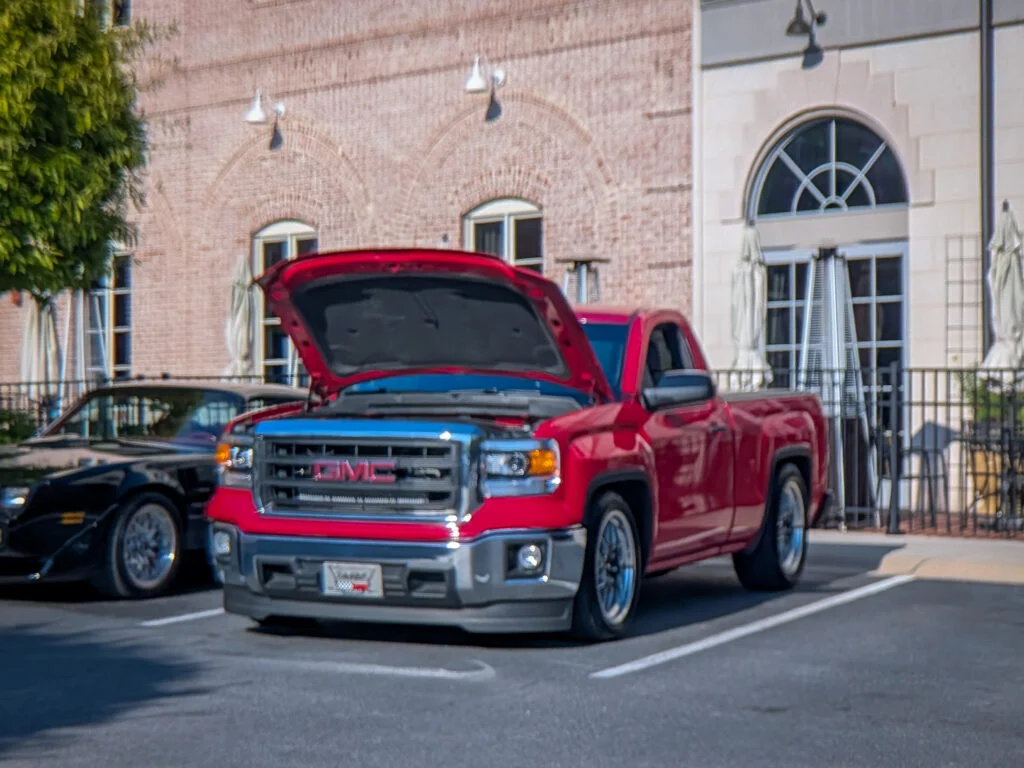 Red GMC pickup truck with hood open at a parking lot near a brick building during daytime