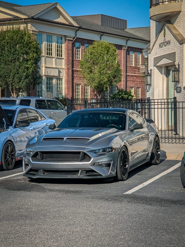 Silver Ford Mustang GT parked in front of brick and stone buildings on a sunny day