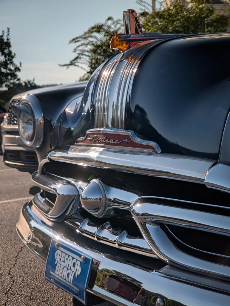 Close-up of the front grille and hood ornament of a black Pontiac Chieftain Station Wagon at an outdoor car event during daytime.