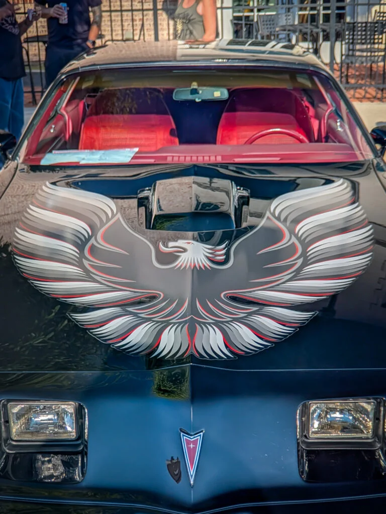 Black Pontiac Firebird with a large silver and red phoenix decal on the hood, showing red interior through windshield