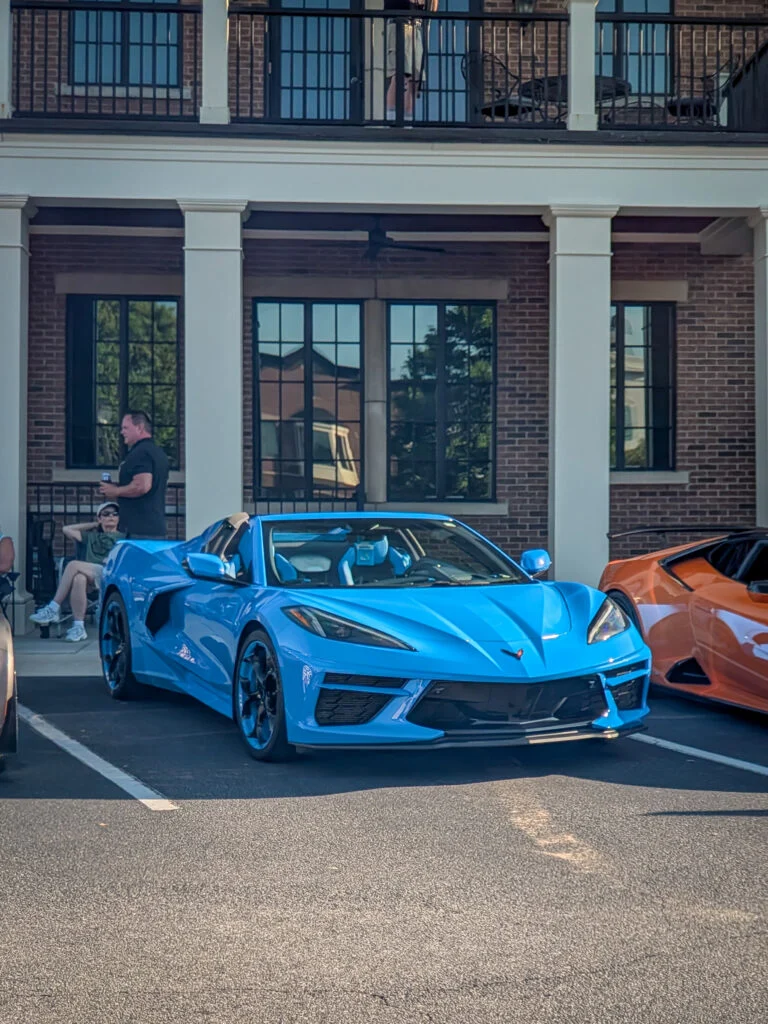 Blue Chevrolet Corvette convertible parked in front of a brick building with people nearby