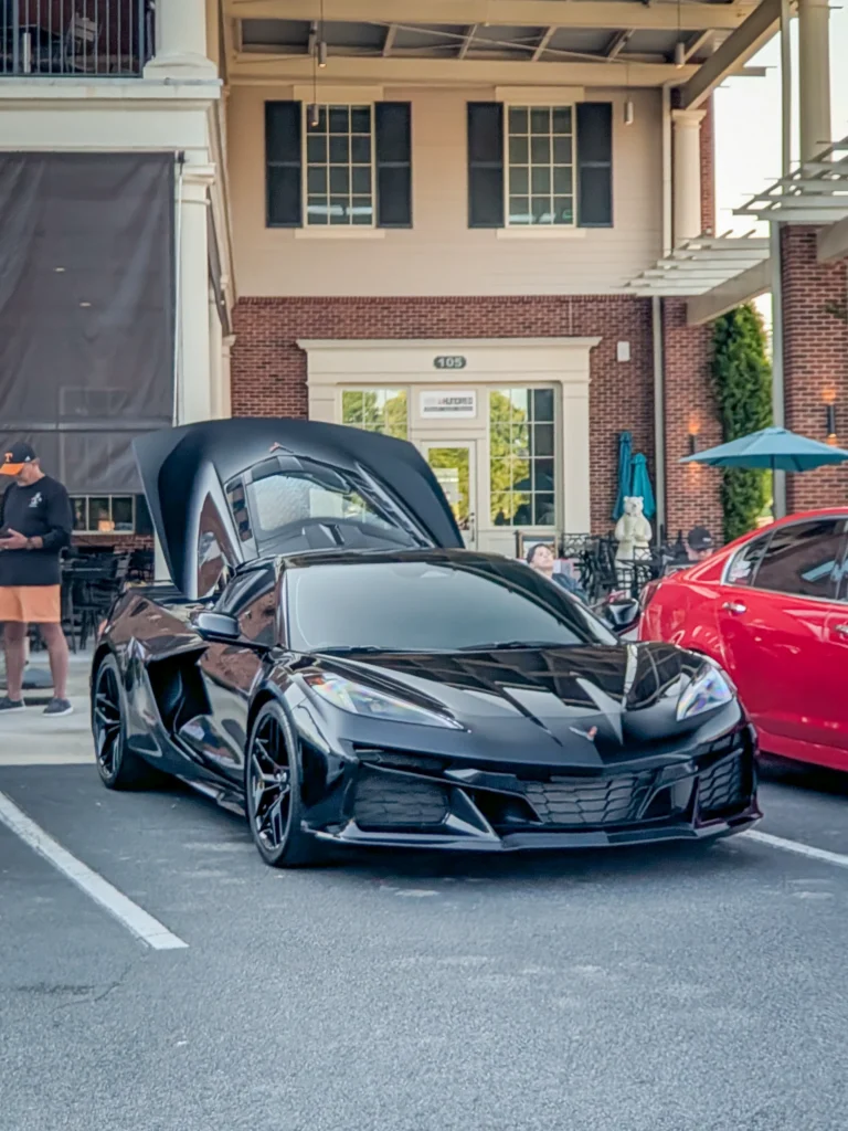 Black Chevrolet Corvette with open hood parked in front of a brick building at a car event