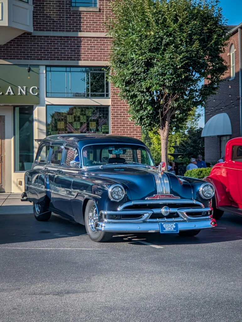 Dark blue Pontiac Chieftain Station Wagon parked on a street in front of a brick building and a tree