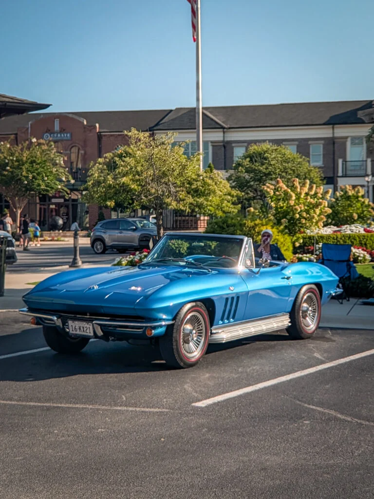 Blue Chevrolet Corvette convertible parked in a lot with trees and buildings in the background