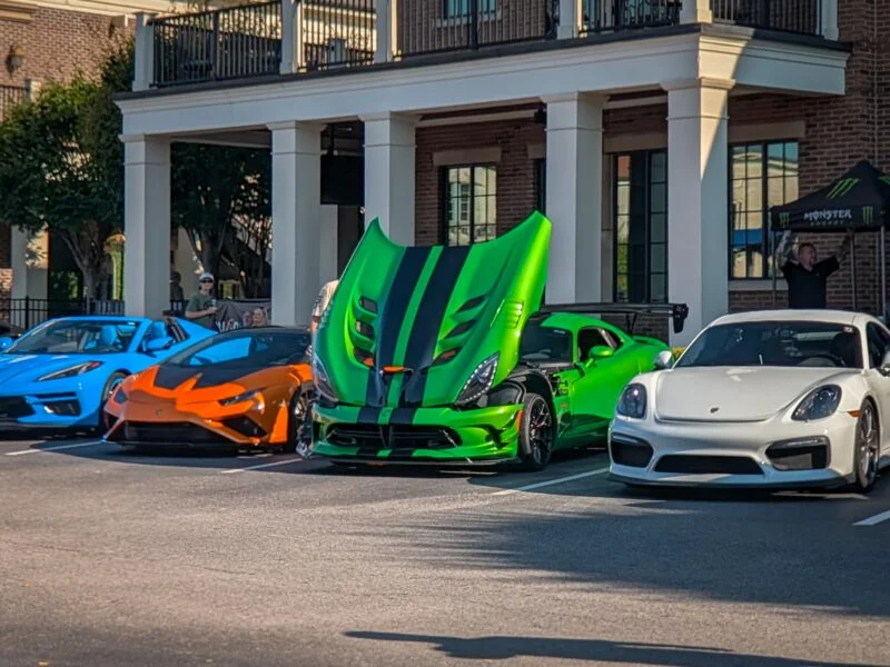 Blue Chevrolet Corvette, orange Lamborghini Huracan, green Dodge Viper with hood open, and white Porsche Cayman parked in fron