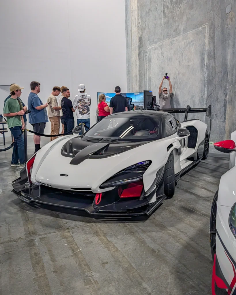 White and black McLaren Senna indoors with people standing around near another white vehicle