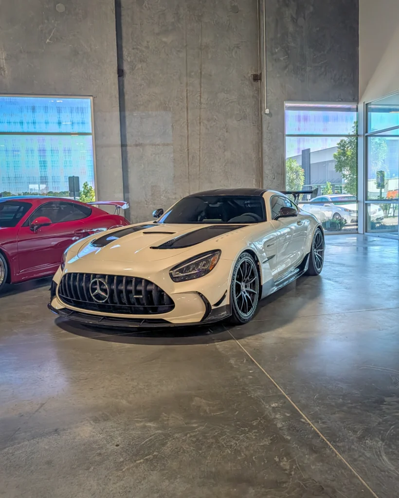 White Mercedes-AMG GT Black Series with black racing stripes and a red sports car in the background inside a showroom