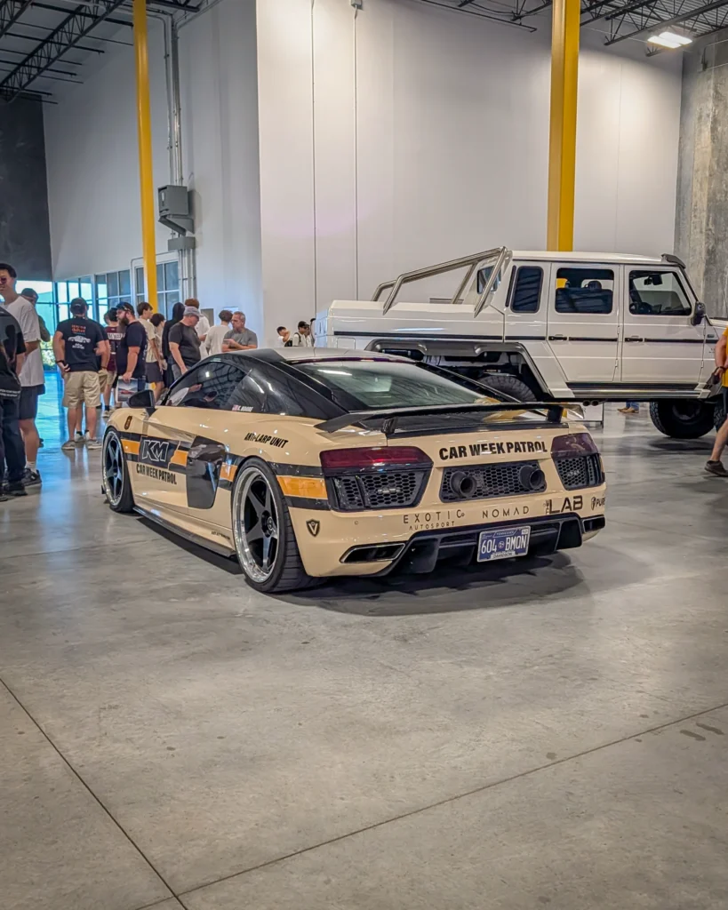 Two vehicles inside a warehouse with people nearby, including a cream Audi R8 with black roof and decals and a white