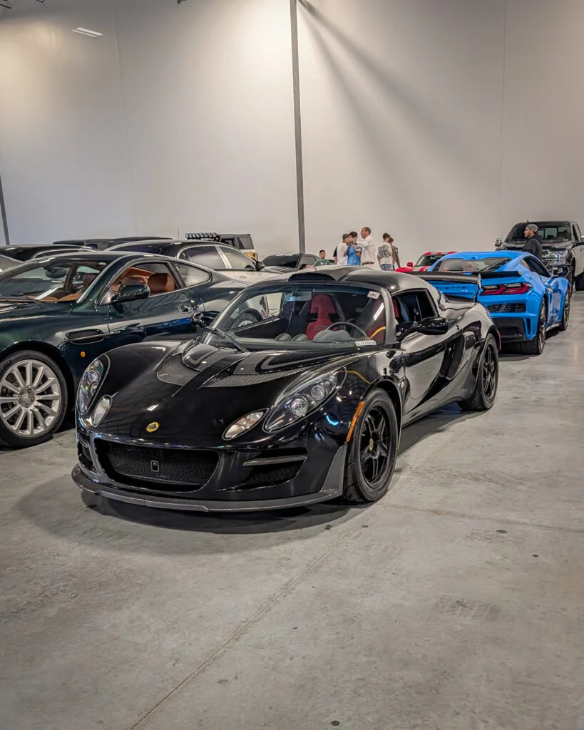 Black Lotus Elise coupe parked indoors with other cars and people in background