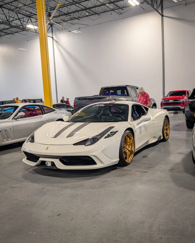 White Ferrari 458 Italia with gold wheels parked indoors with other vehicles and a person standing nearby