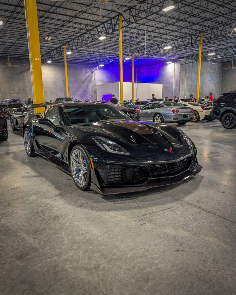 Black Chevrolet Corvette ZR1 parked indoors at a car event with other sports cars and people in the background