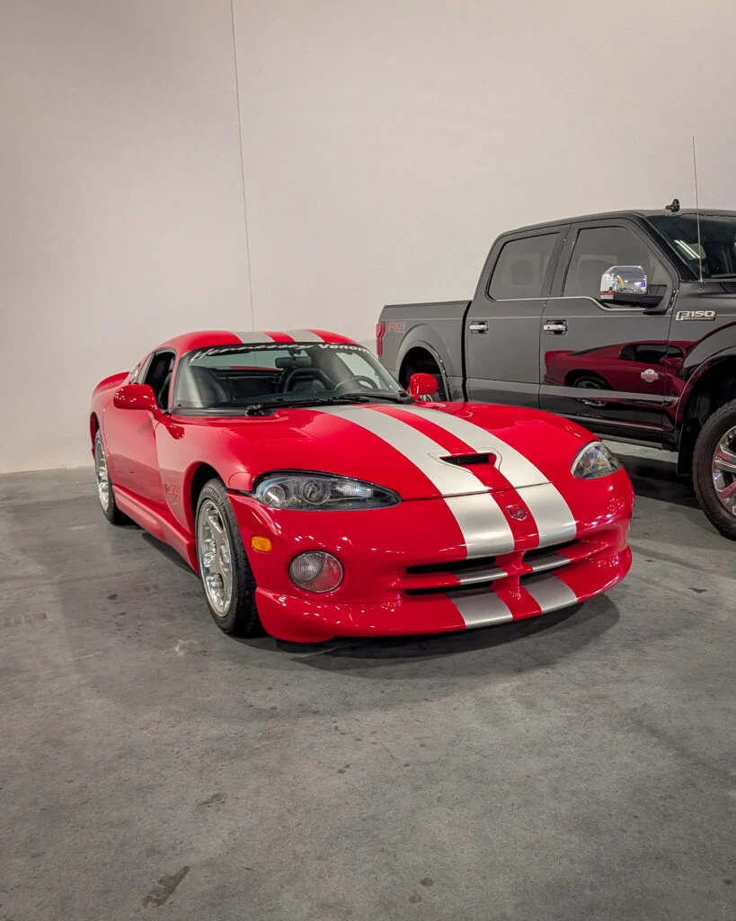 Red Dodge Viper with white stripes parked indoors next to a dark gray Ford F-150 pickup truck.